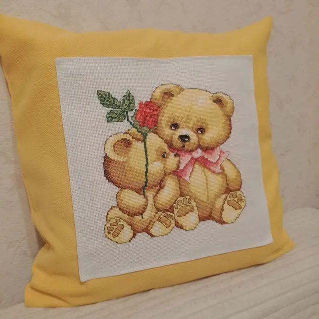 Decorative pillow case in mustard color with a couple of teddy bears embroidered with a cross