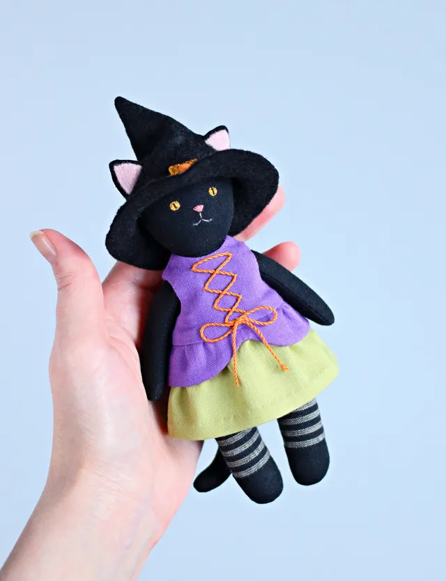 Look how cute this tiny Halloween cat is! It's wearing a witch costume: a medieval dress with a lace-up front and a peplum, a pointed wide brim hat, and striped tights! Why not sew this softie yourself and use it as a Boo basket filler? It's quick and easy with my sewing pattern!