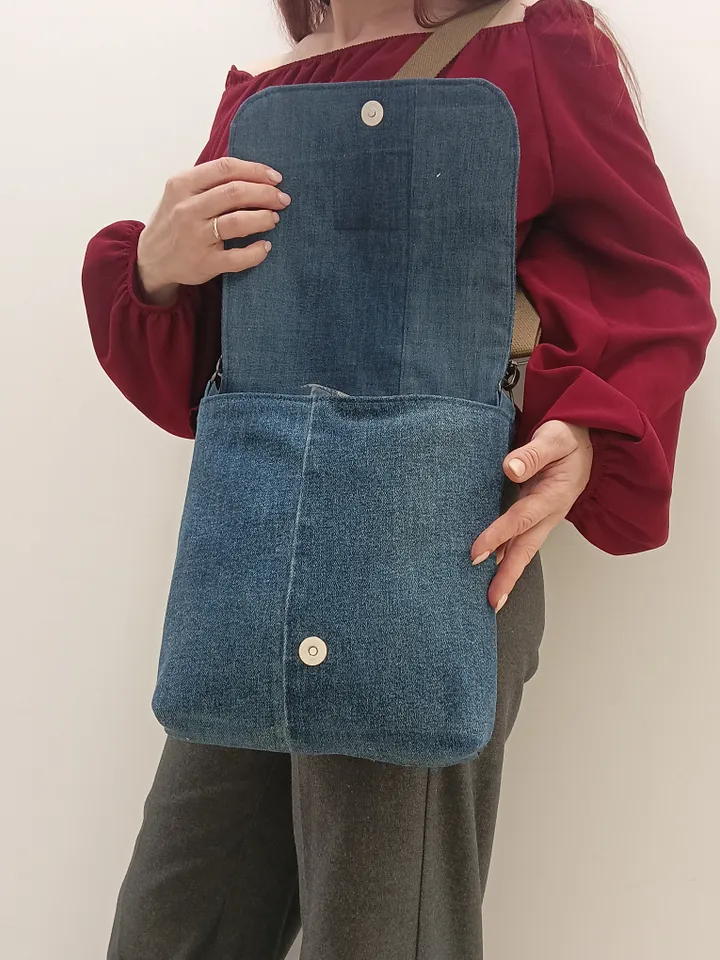Denim messenger bag made of denim fabric with a denim belt flap. It has an external pocket on the back wall, 3 internal pockets and a patterned cotton lining.