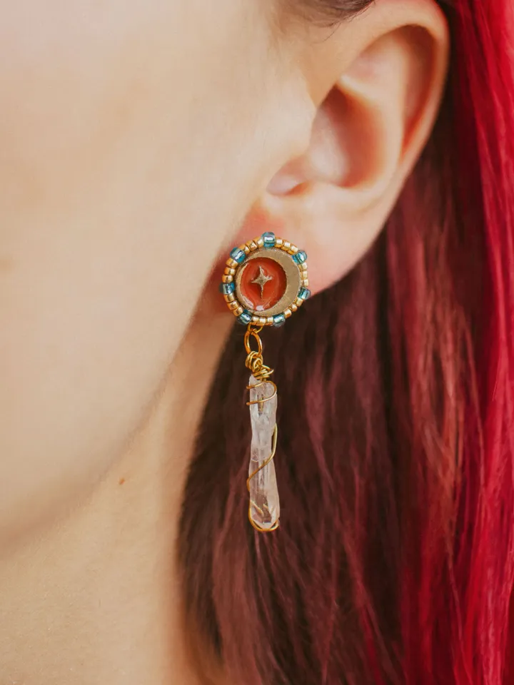 Asymmetrical stud earrings When The Sun Meets The Moon with clear quartz crystals. Gold jewelry with celestial design in sunset red and orange color with beading. Maylina Soul