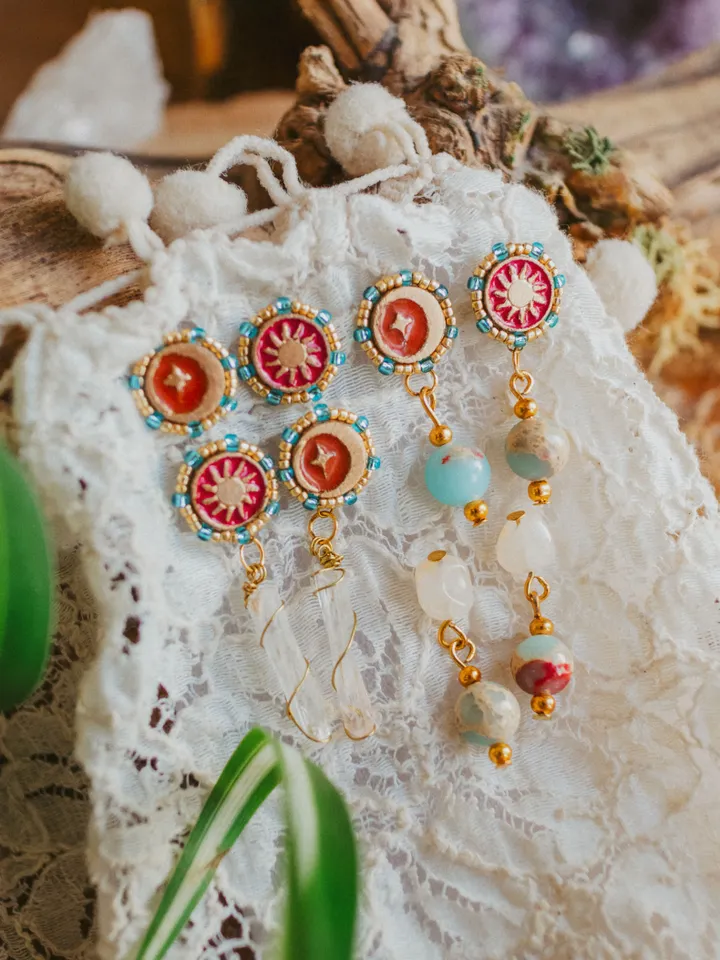 Asymmetrical stud earrings When The Sun Meets The Moon with clear quartz crystals. Gold jewelry with celestial design in sunset red and orange color with beading. Maylina Soul