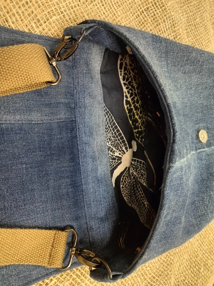 Denim messenger bag made of denim fabric with a denim belt flap. It has an external pocket on the back wall, 3 internal pockets and a patterned cotton lining.