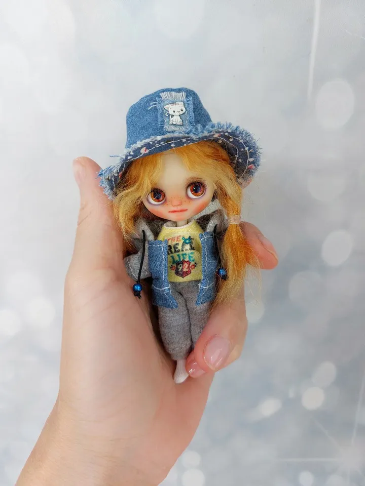 A little Blythe doll with red hair and brown eyes. a girl in a denim outfit.