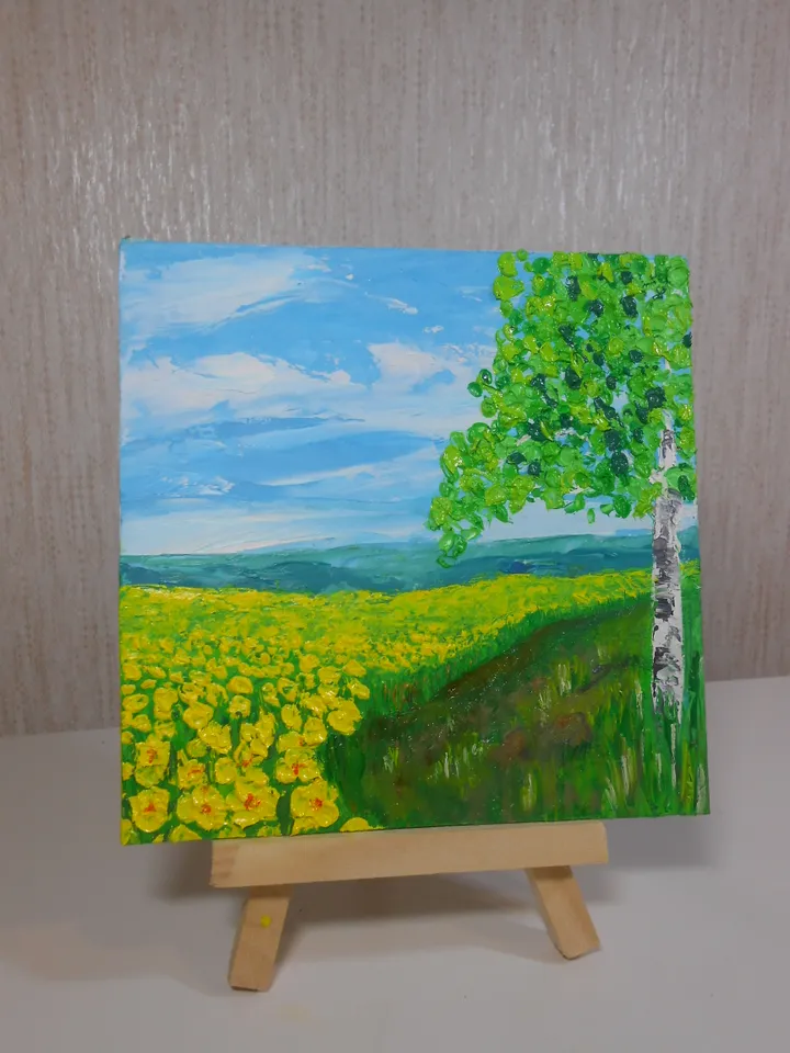 A bright landscape. Mountains in the distance, blue sky with light clouds, a field of yellow flowers, a birch tree. The original painting.