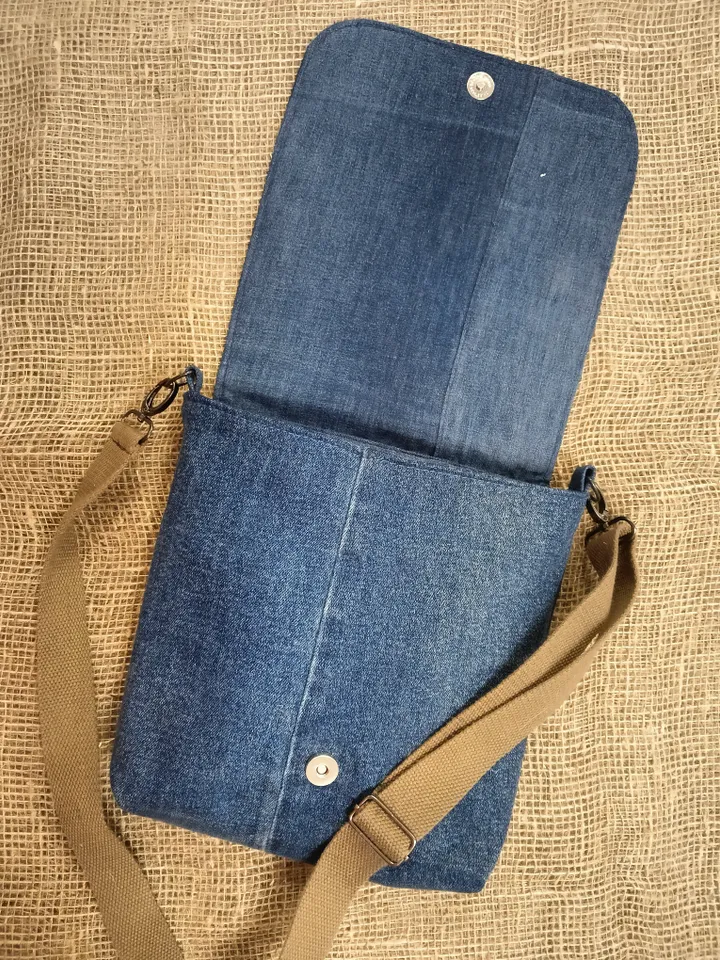 Denim messenger bag made of denim fabric with a denim belt flap. It has an external pocket on the back wall, 3 internal pockets and a patterned cotton lining.