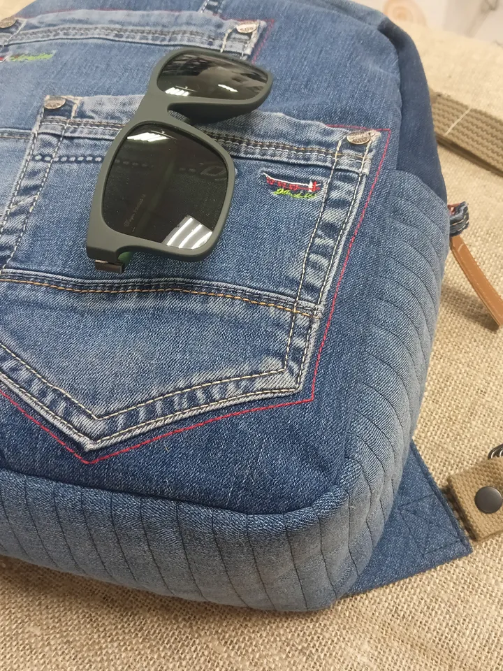 Casual unisex denim backpack made from recycled jeans, with 3 pockets outside and 3 pockets inside (1 with a zipper), strong 2-color strap on adjustable straps. Inside is synthetic fabric. The back and bottom is quilted.
