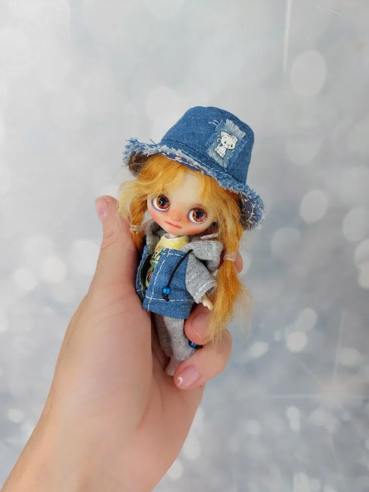 A little Blythe doll with red hair and brown eyes. a girl in a denim outfit.