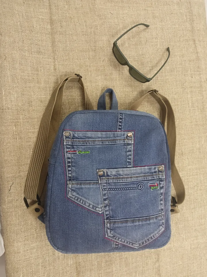 Casual unisex denim backpack made from recycled jeans, with 3 pockets outside and 3 pockets inside (1 with a zipper), strong 2-color strap on adjustable straps. Inside is synthetic fabric. The back and bottom is quilted.