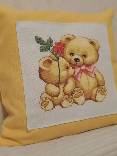Decorative pillow case in mustard color with a couple of teddy bears embroidered with a cross