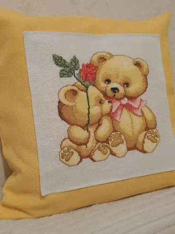 Decorative pillow case in mustard color with a couple of teddy bears embroidered with a cross